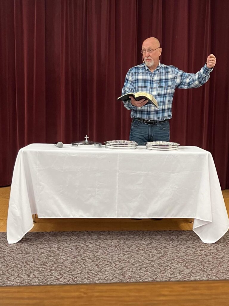 Pastor Gary page standing by communion table